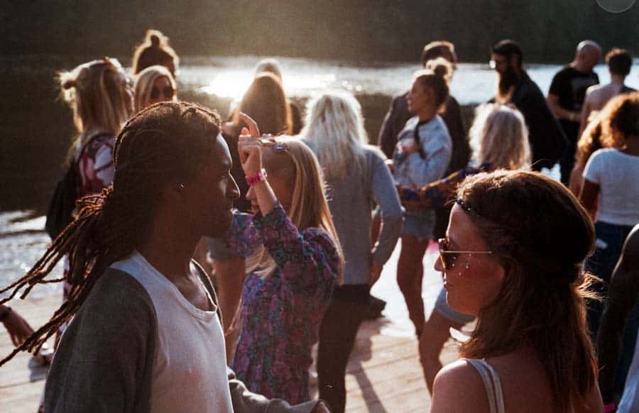 People dancing outdoors by water at sunset.