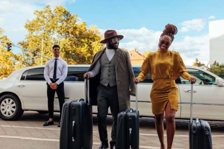 Stylish couple with luggage exiting limousine with chauffeur