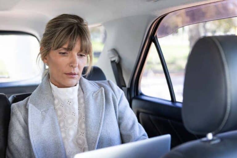 Woman using laptop in backseat of car