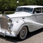 White vintage Rolls-Royce sedan parked on a sunny street