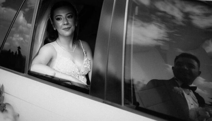 Bride in car window, groom reflected beside her