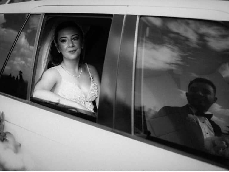 Bride in car window, groom reflected beside her