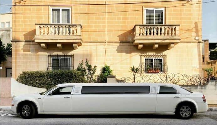 White stretch limousine parked before beige stone house