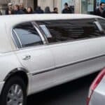 White stretch limousine driving past city pedestrians
