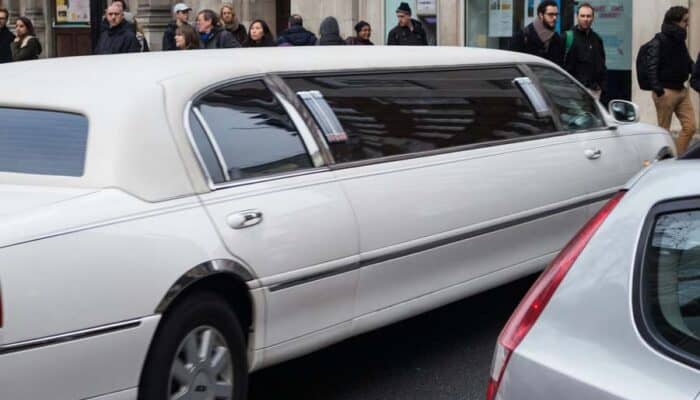 White stretch limousine driving past city pedestrians