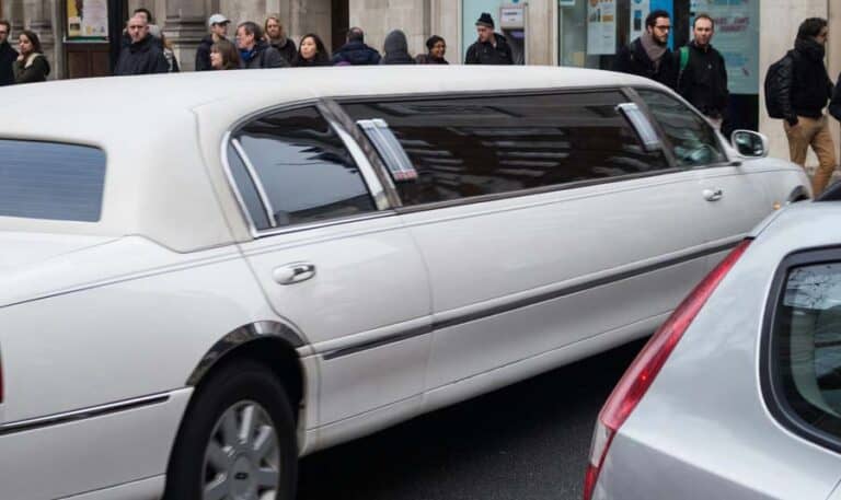 White stretch limousine driving past city pedestrians