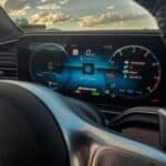 Digital car dashboard display at sunset behind steering wheel