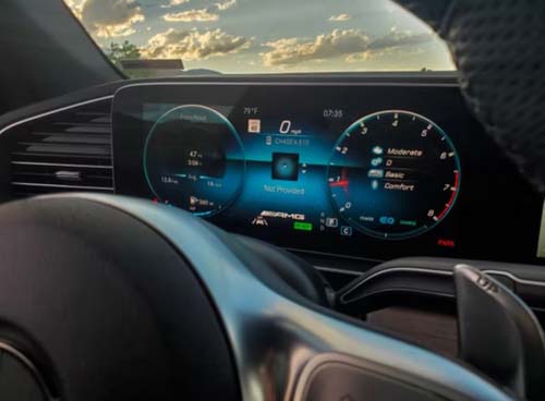 Digital car dashboard display at sunset behind steering wheel