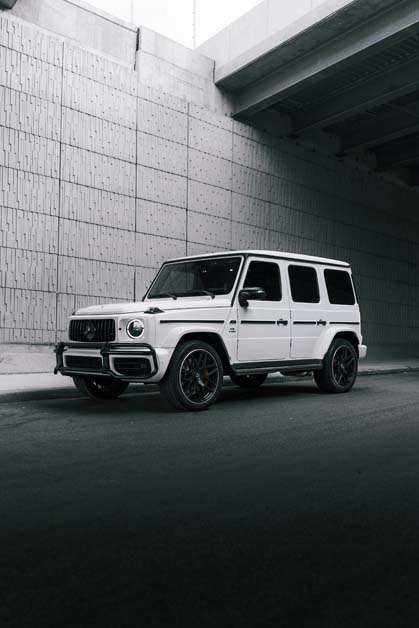 White Mercedes G-Wagen SUV parked under urban overpass.