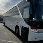 White coach bus parked in a lot under cloudy sky