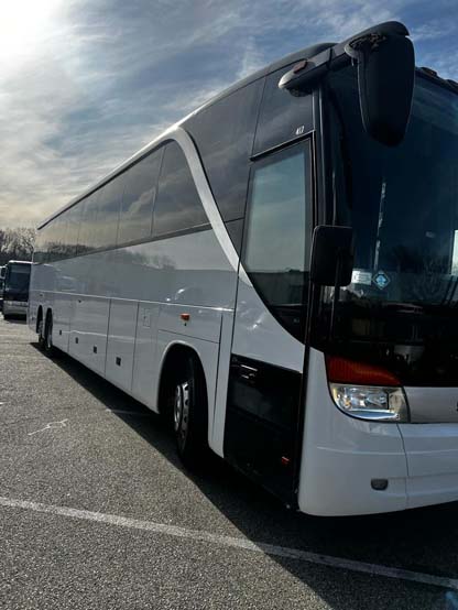 White coach bus parked in a lot under cloudy sky
