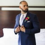 Man in navy suit with boutonniere adjusting jacket