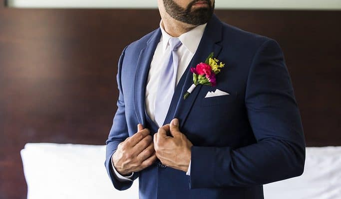 Man in navy suit with boutonniere adjusting jacket
