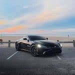 Black sports car parked by beach at sunset