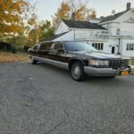Black stretch limousine parked outside white house in autumn