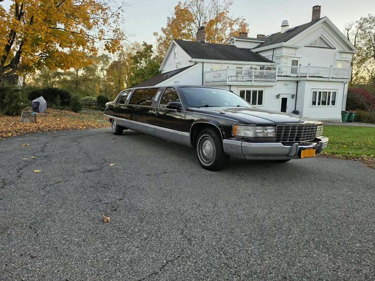 Black stretch limousine parked outside white house in autumn