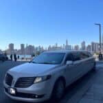 White stretch limousine parked by city skyline waterfront