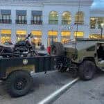 Military-style Humvee towing motorcycle trailer outside mall store