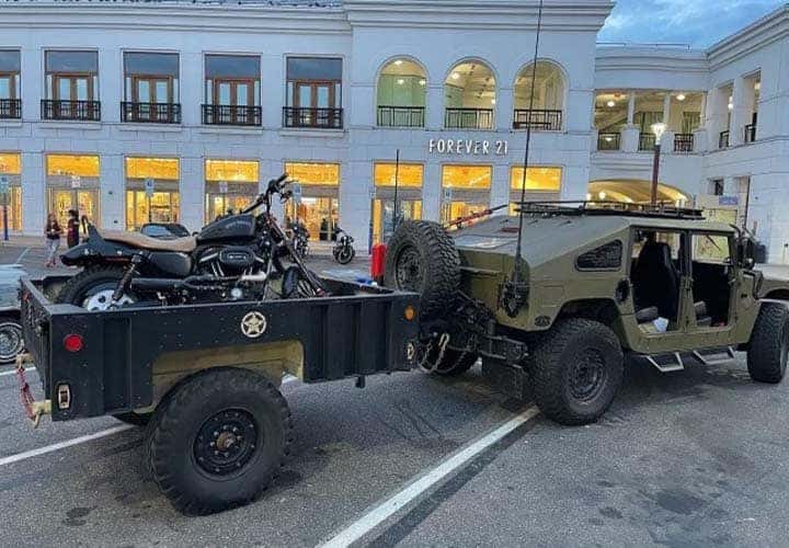 Military-style Humvee towing motorcycle trailer outside mall store