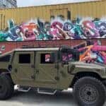 Military-style armored vehicle parked before colorful graffiti containers