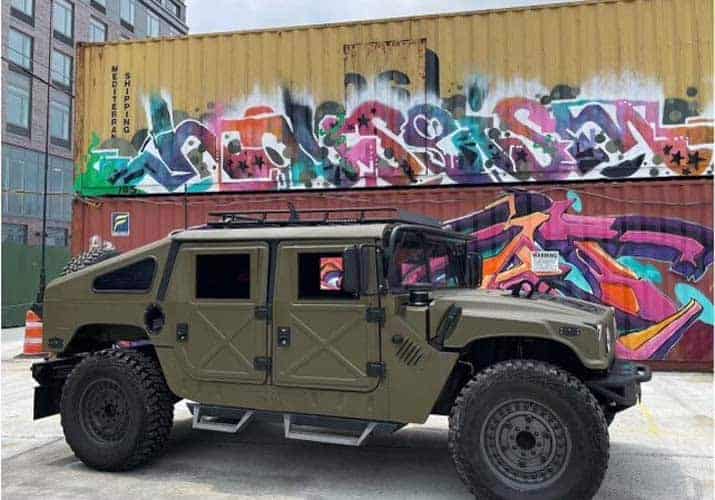 Military-style armored vehicle parked before colorful graffiti containers