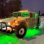 Humvee with green underglow lights on snowy road at night
