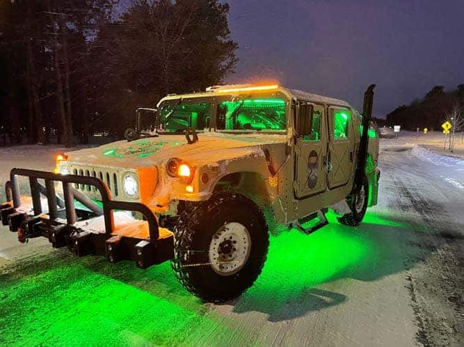 Humvee with green underglow lights on snowy road at night