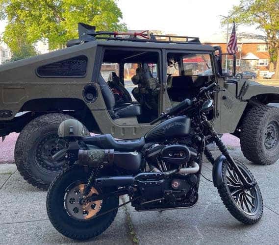 Black motorcycle parked before military-style Humvee vehicle