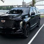 Black Cadillac Escalade parked beside river with bridge behind