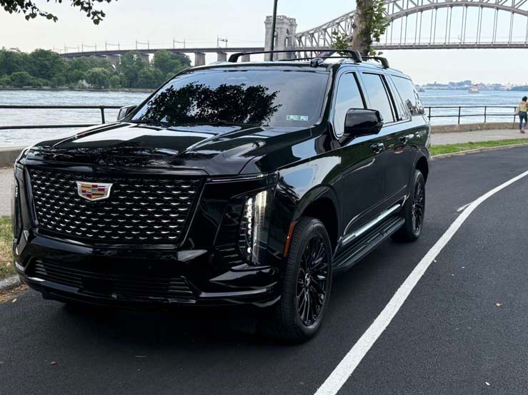 Black Cadillac Escalade parked beside river with bridge behind