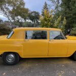 Classic yellow Checker car parked outdoors on a cloudy day.
