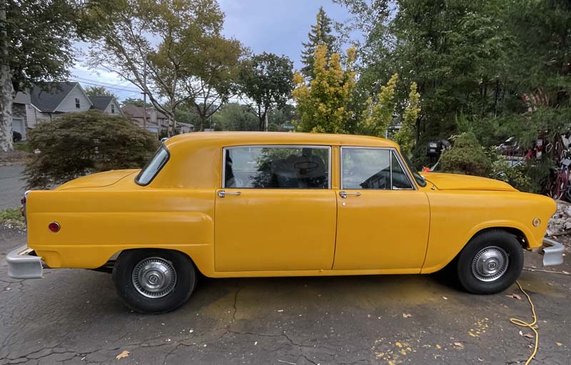 Classic yellow Checker car parked outdoors on a cloudy day.