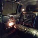 Luxurious limousine interior with black leather seating and wood paneling.