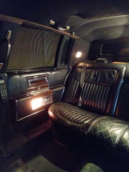 Luxurious limousine interior with black leather seating and wood paneling.