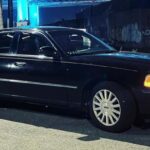 Black sedan limousine parked at night with headlights on
