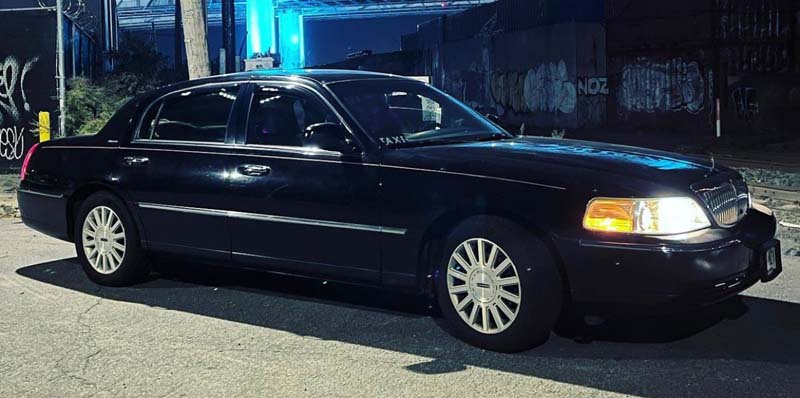 Black sedan limousine parked at night with headlights on