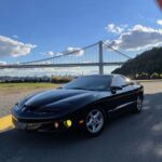 Black sports car parked near suspension bridge.