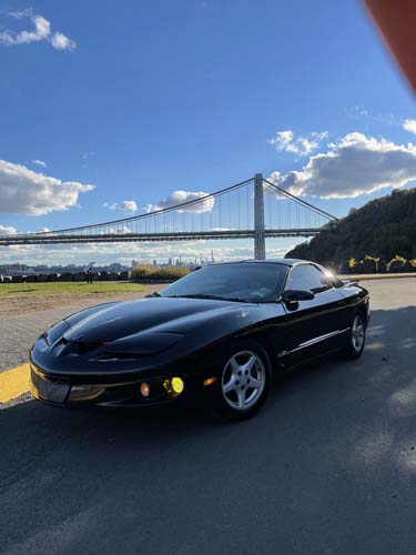 Black sports car parked near suspension bridge.