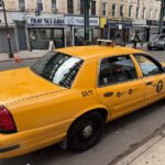 NYC yellow taxi cab on a street with buildings.