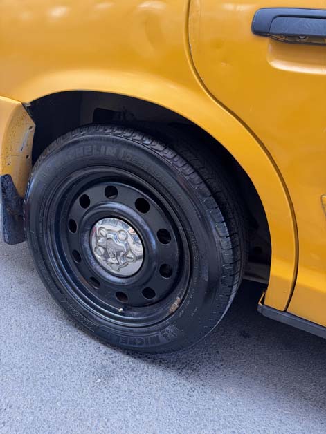 Close-up of a yellow taxi's rear wheel and Michelin tire.