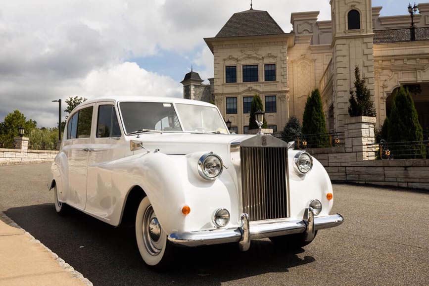 Vintage white Rolls-Royce parked in front of a grand mansion.