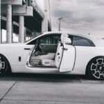 White Rolls-Royce Wraith with open doors under a bridge.