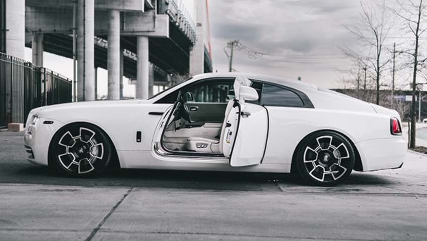 White Rolls-Royce Wraith with open doors under a bridge.