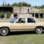 Beige vintage sedan parked before abandoned concrete building